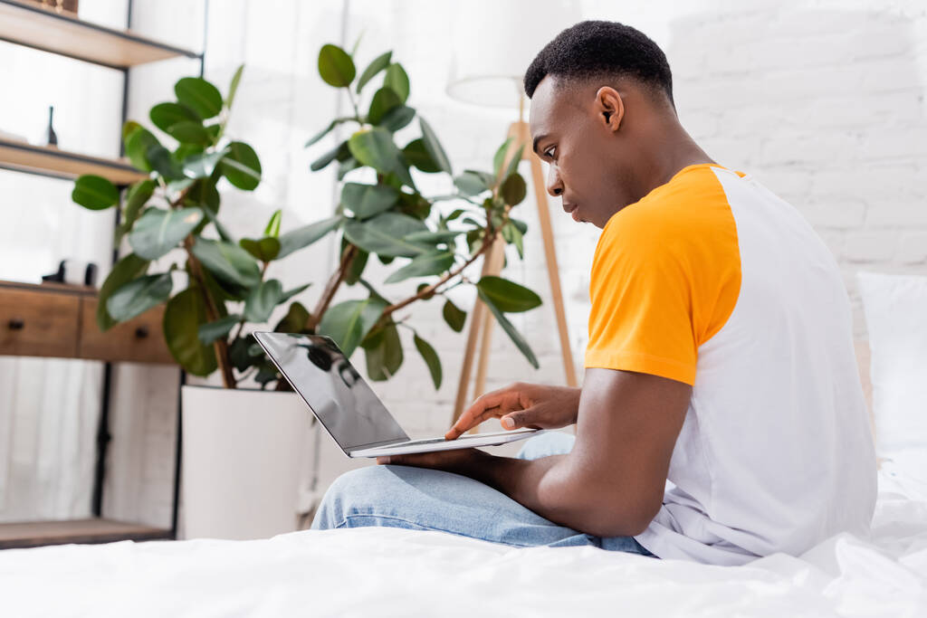 Genç Afro-Amerikan adam yatak odasında boş ekranlı dizüstü bilgisayar kullanıyor.  - Fotoğraf, Görsel