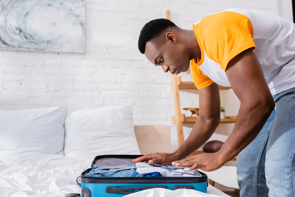 Afrikai amerikai férfi ruhákat tesz bőröndbe otthon az ágyon.  - Fotó, kép