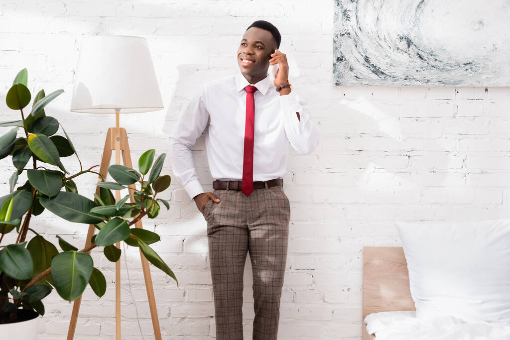 Homme d'affaires afro-américain souriant parlant sur smartphone près du lampadaire dans la chambre  - Photo, image