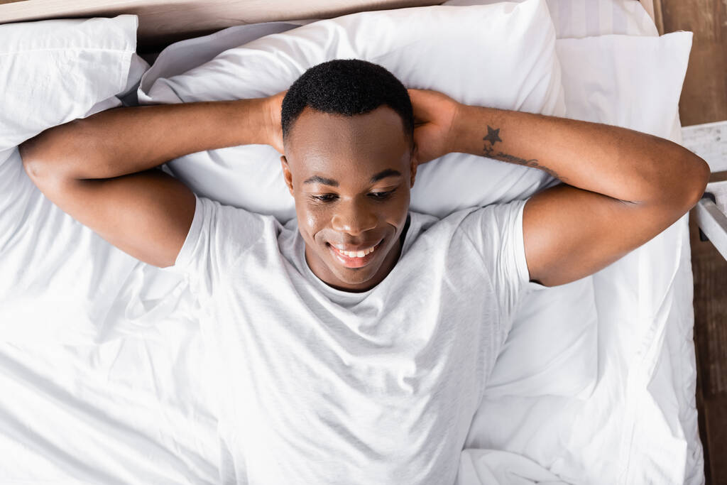 Κάτοψη του χαμογελαστού Αφροαμερικανού ξαπλωμένου στο κρεβάτι  - Φωτογραφία, εικόνα