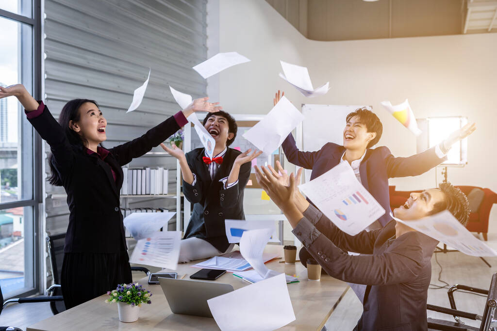 Успешные счастливые работники Группа азиатских бизнесменов с разным полом (ЛГБТ) подбросила бизнес-план на бумаге в воздух в конференц-зале в офисе, эмоционально удовлетворенная - Фото, изображение