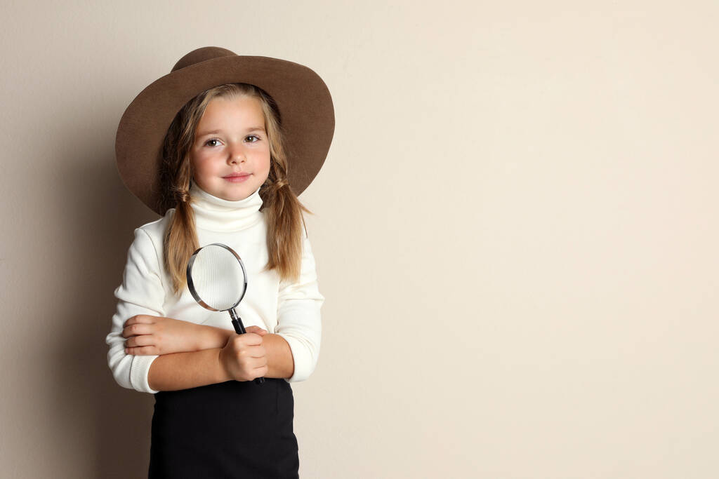 Cute little child in hat with magnifying glass playing detective on beige background, space for text - Photo, Image