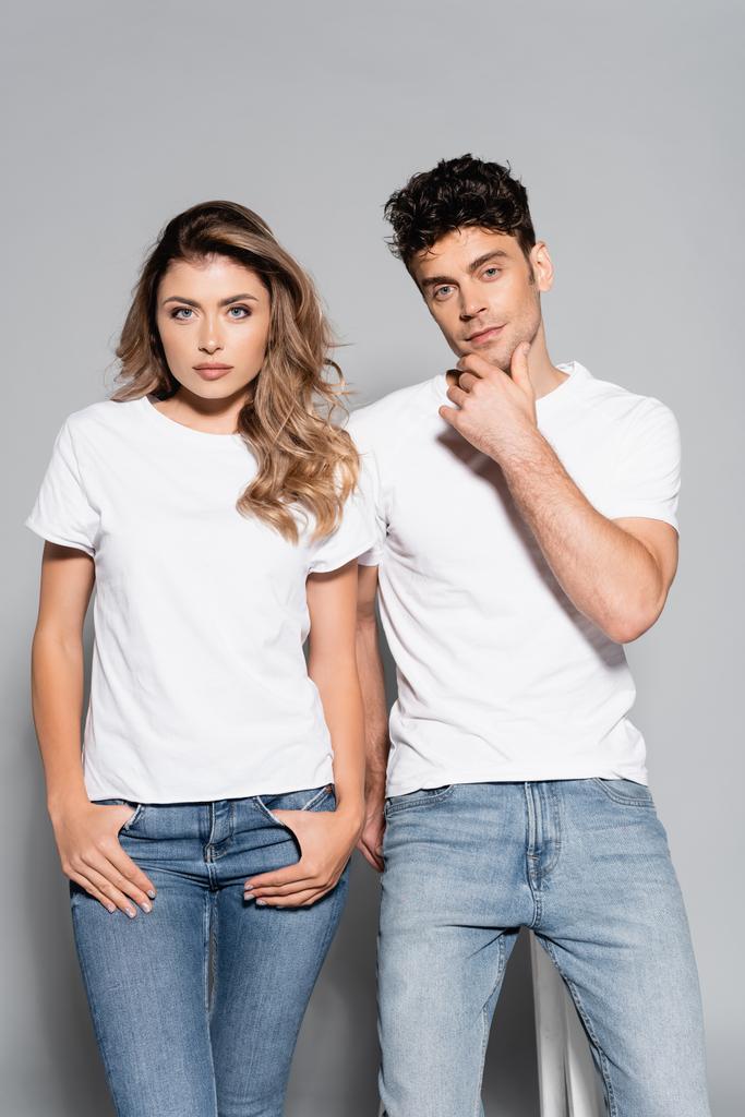 jovem casal em camisetas brancas e jeans posando isolado em cinza - Foto, Imagem