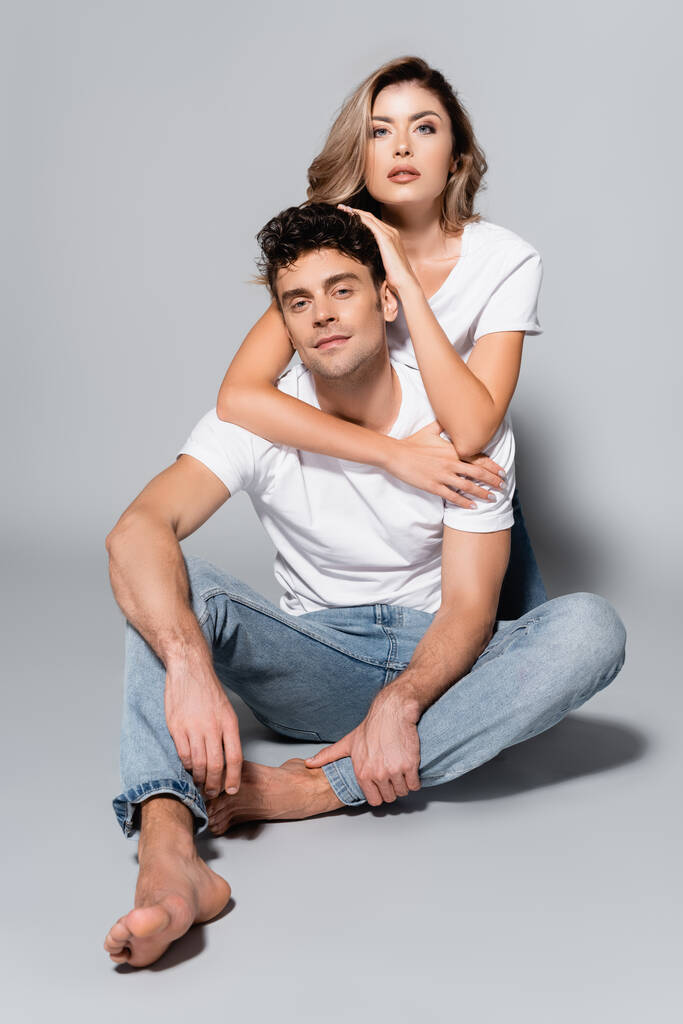 joven pareja en blanco camisetas abrazando aislado en gris - Foto, imagen