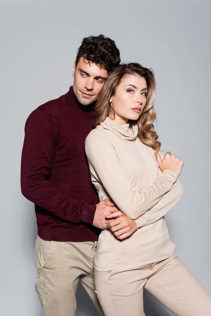 casual young couple in turtleneck jumpers embracing isolated on grey - Photo, Image
