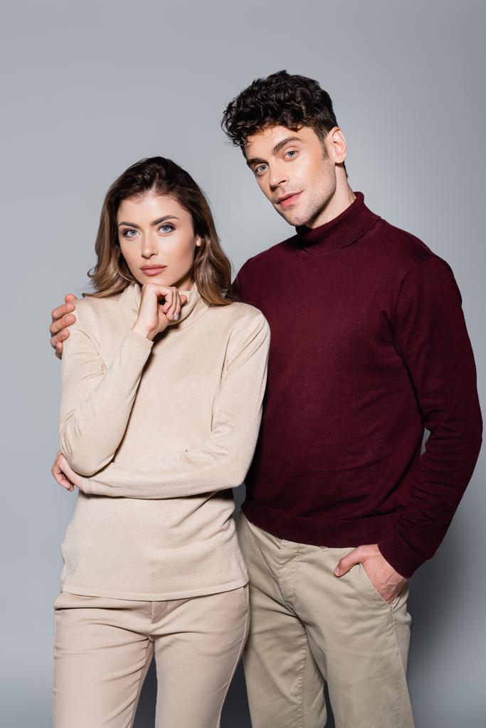 casual joven pareja en jerséis posando aislado en gris - Foto, imagen
