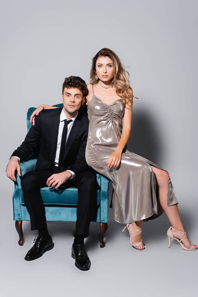 elegantes junges Paar posiert in Velours-Sessel isoliert auf grau - Foto, Bild