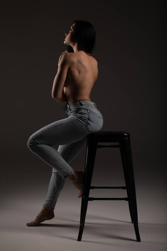 Zamyšlená brunetka bez trička s dlouhými vlasy pózující opřený o bar židle - Fotografie, Obrázek