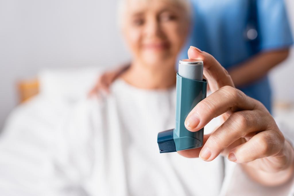 aged woman holding inhaler near nurse in hospital, blurred background - Photo, Image