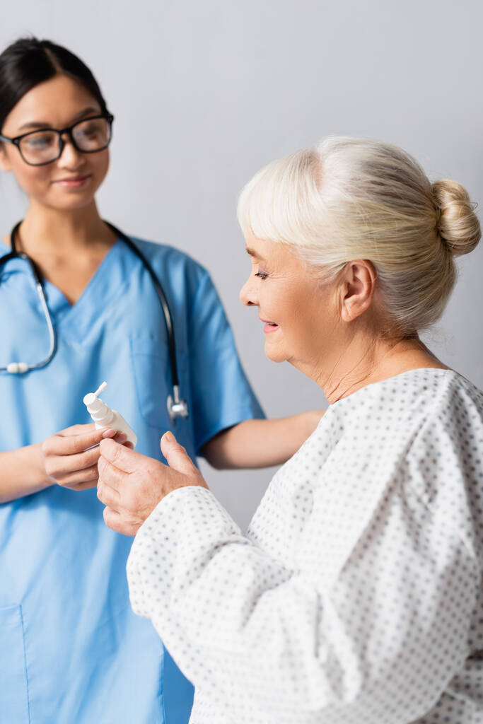 young asian nurse giving nasal spray to senior woman, blurred background - Photo, Image