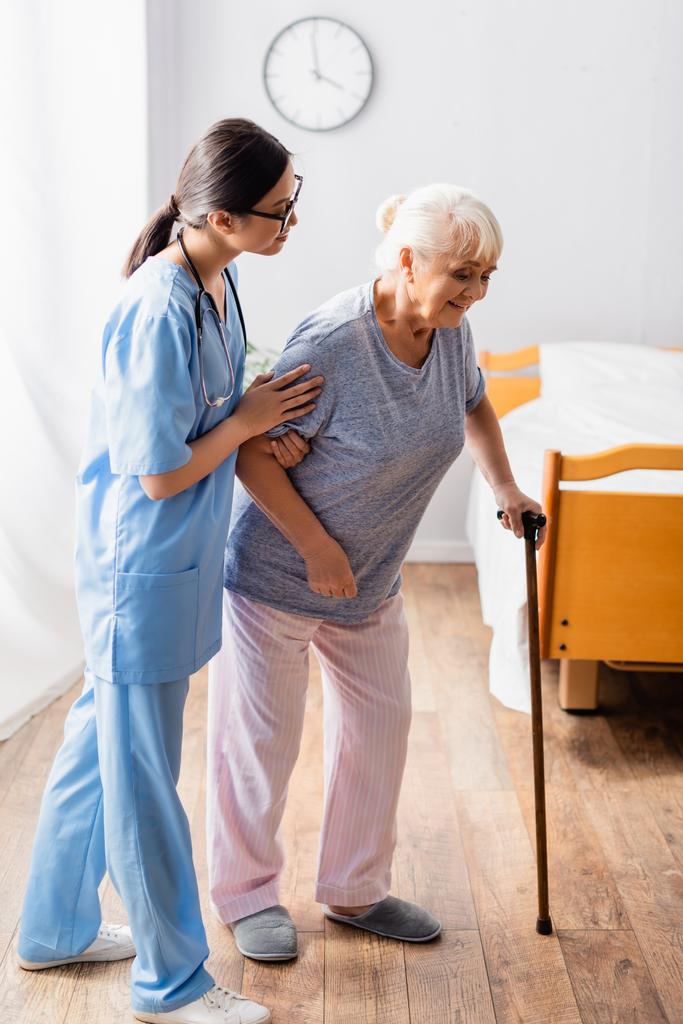 aziatische verpleegster helpen oud vrouw wandelen met stok in ziekenhuis - Foto, afbeelding