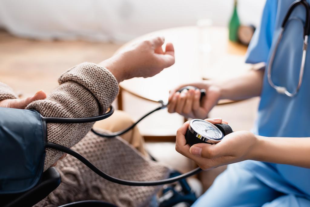 高齢女性の血圧を測定する若い看護師の部分的見解背景のぼやけ - 写真・画像