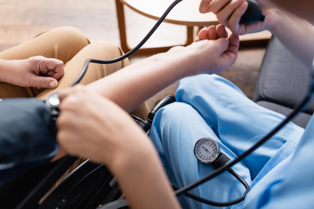 обрізаний вид медсестри, що вимірює кров'яний тиск літньої жінки, розмитий передній план
 - Фото, зображення