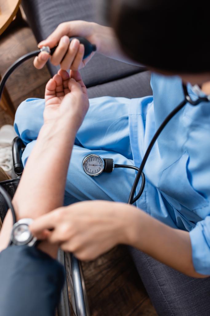 visão recortada da enfermeira que mede a pressão arterial da mulher idosa com tonômetro, visão frontal turva - Foto, Imagem