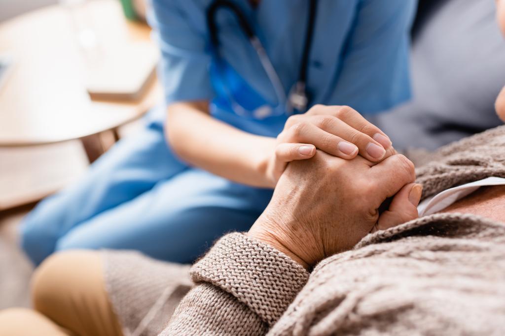 partial view of nurse touching hands of aged patient in nursing home, blurred background - Photo, Image