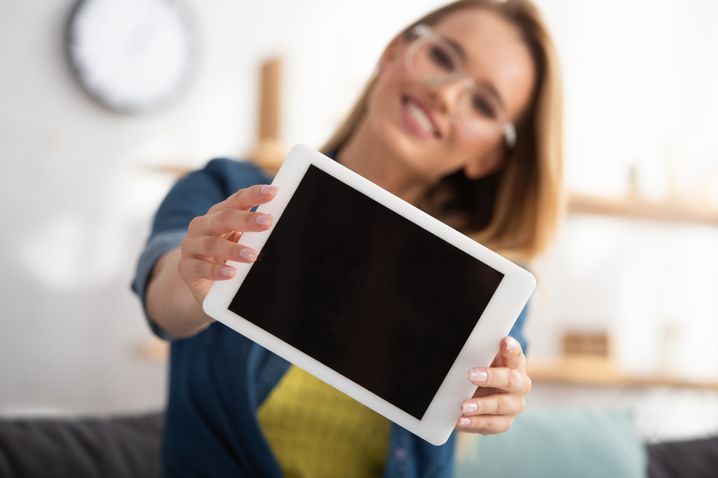 gelukkig blond vrouw kijken naar camera terwijl het tonen van digitale tablet op wazig achtergrond - Foto, afbeelding