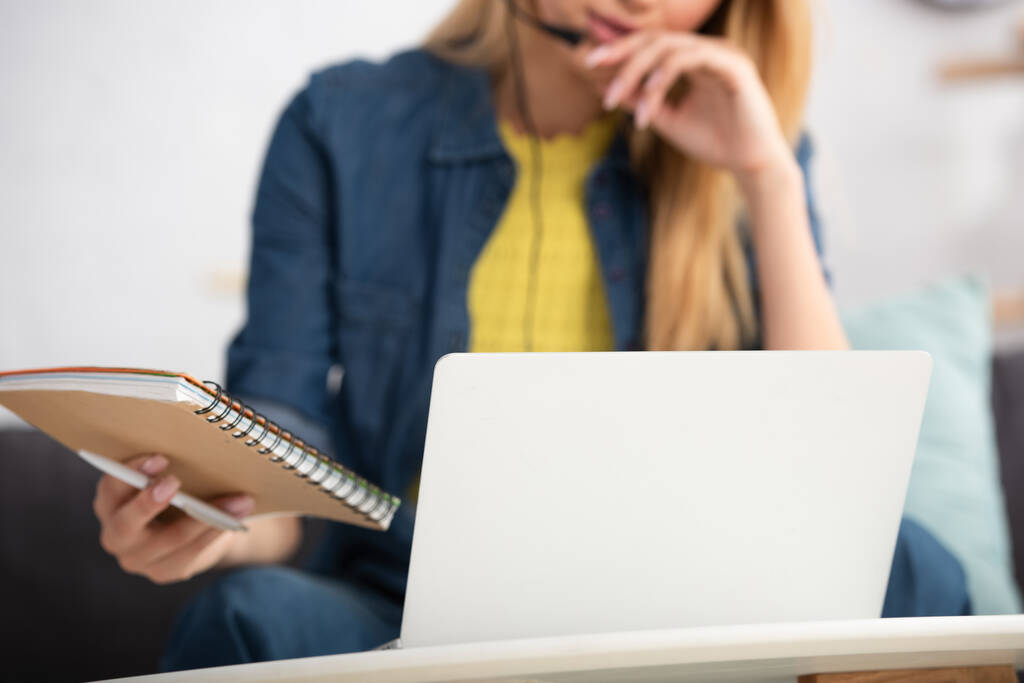 Vista ritagliata di giovane donna in possesso di notebook e penna vicino al computer portatile a casa su sfondo sfocato - Foto, immagini