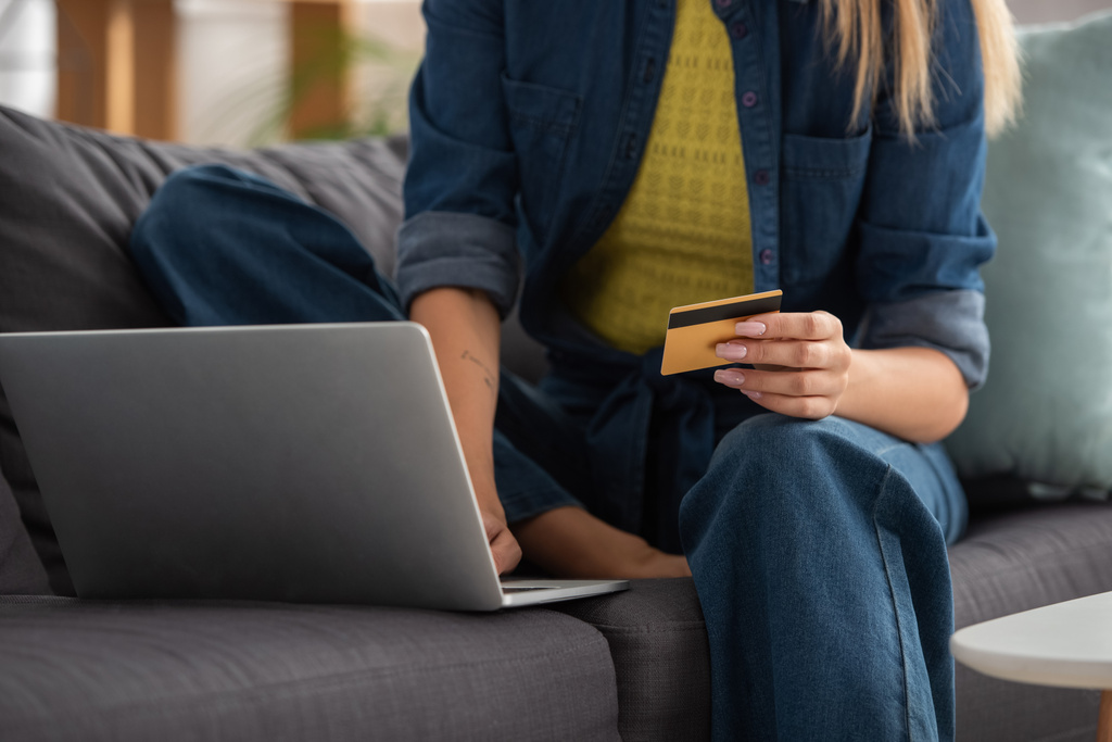 Ausgeschnittene Ansicht einer jungen Frau mit Kreditkarte mittels Laptop auf verschwommenem Hintergrund - Foto, Bild