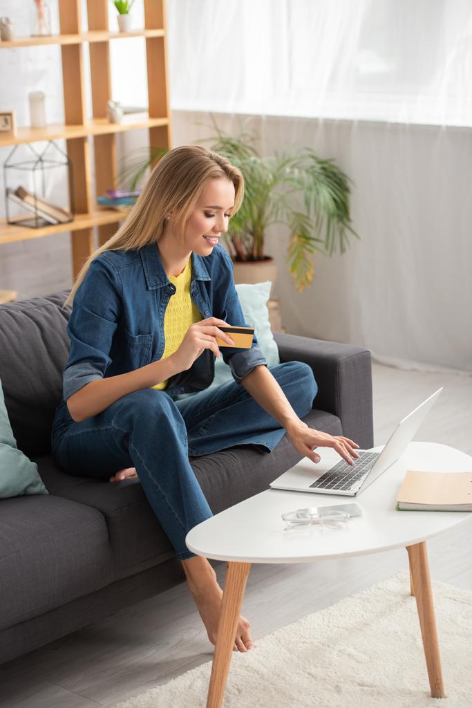 Kredi kartıyla evde bilgisayarında bulanık arka planda yazan mutlu sarışın bir kadın. - Fotoğraf, Görsel