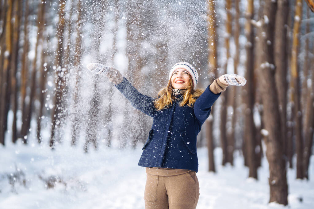 Szczęśliwej zimy. Ładna kobieta bawiąca się śniegiem w śnieżnym lesie. Młoda dama w zimowych ubraniach ciesząca się zimą. Urlop zimowy. - Zdjęcie, obraz