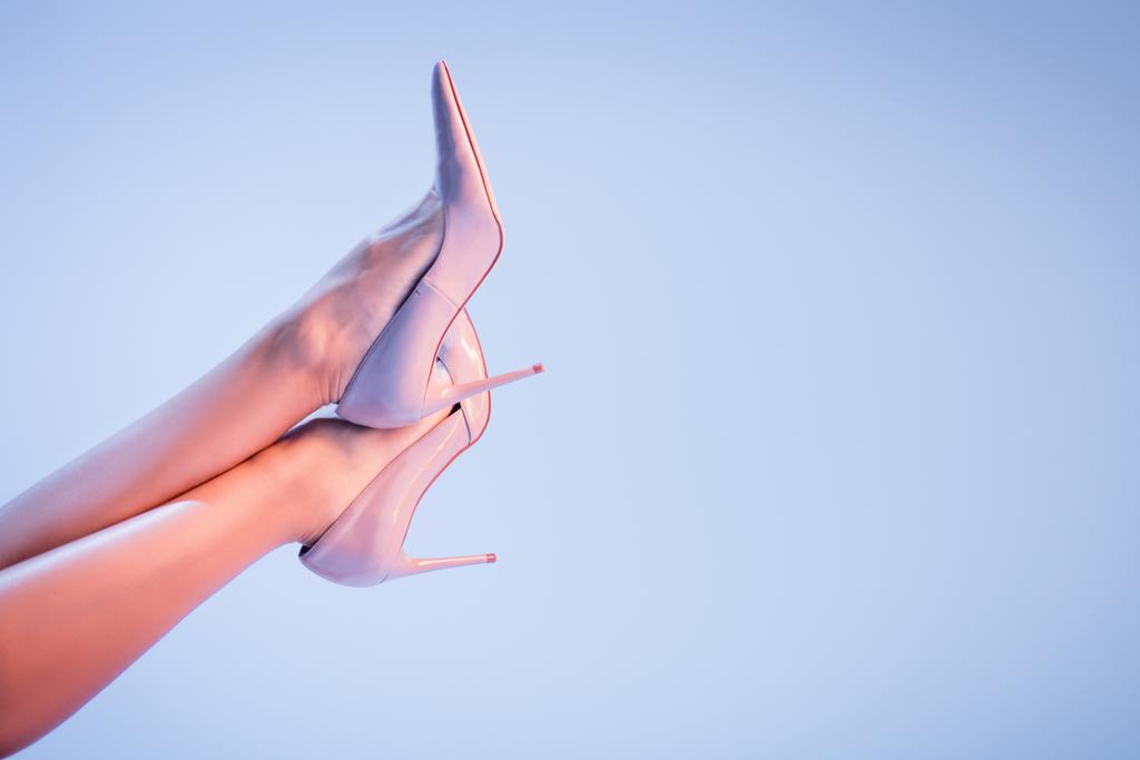 Ausgeschnittene Ansicht der Beine einer jungen Frau in High Heels auf blauem Hintergrund  - Foto, Bild