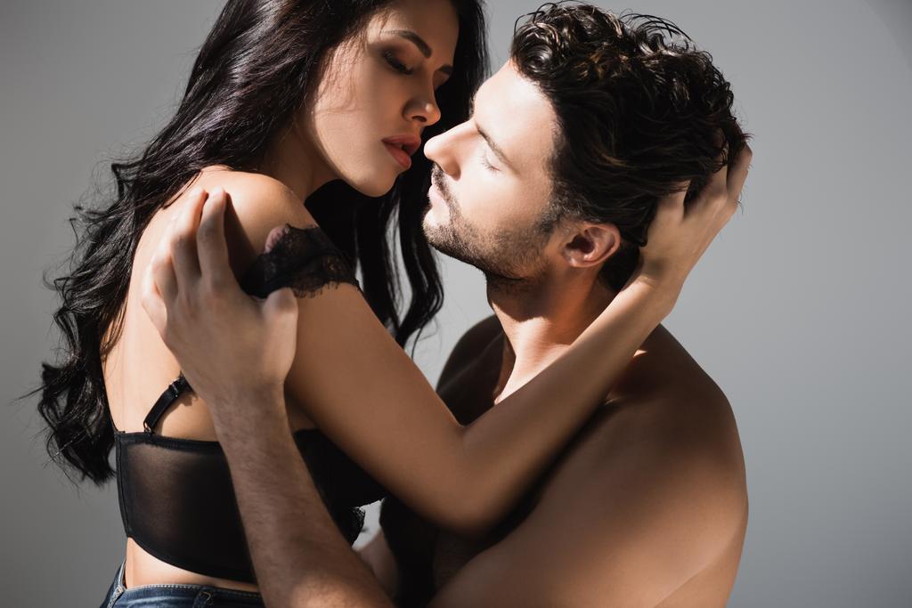 Femme sexy en soutien-gorge embrasser et toucher les cheveux de copain torse nu sur fond gris - Photo, image