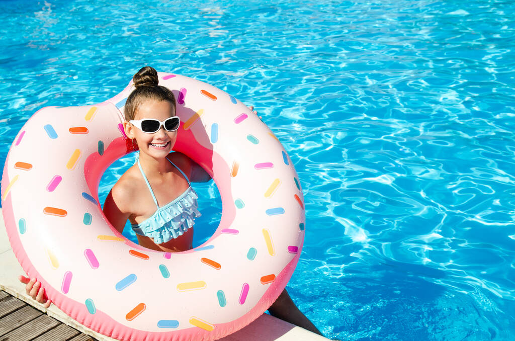 Linda niña sonriente en la piscina con anillo de goma. Niño divirtiéndose de vacaciones en verano - Foto, imagen