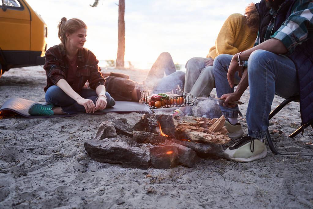 Vrienden zitten op het strand rond het kampvuur - Foto, afbeelding