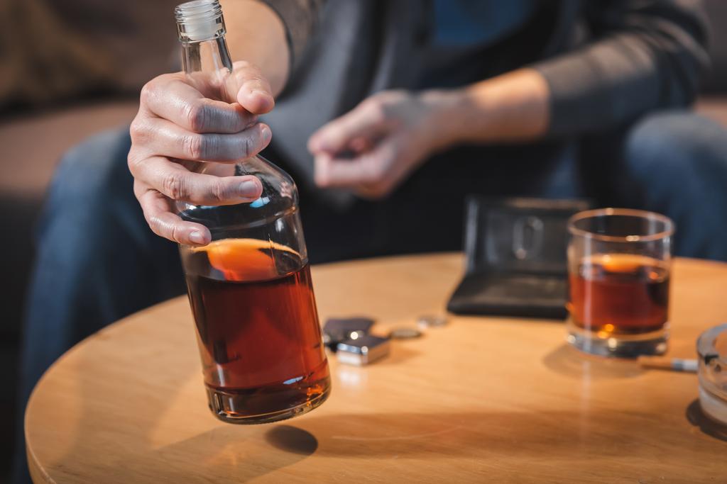 részleges kilátás alkohol-függő férfi gazdaság üveg whisky, homályos háttér - Fotó, kép
