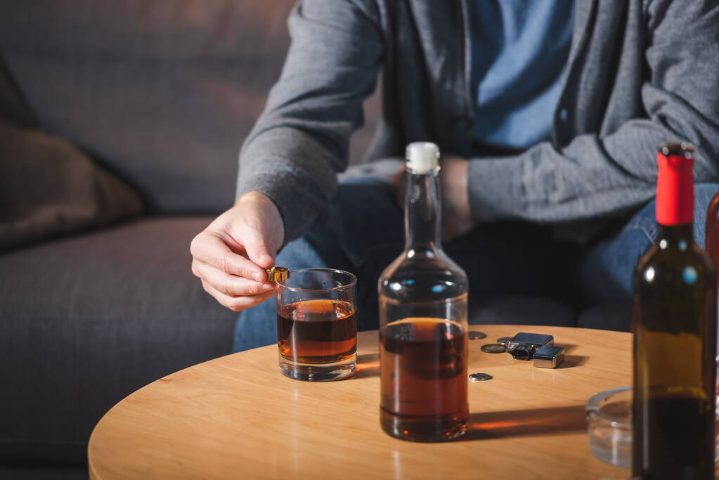 bijgesneden weergave van de man met trouwring in de buurt van glas en fles whisky, wazig achtergrond - Foto, afbeelding