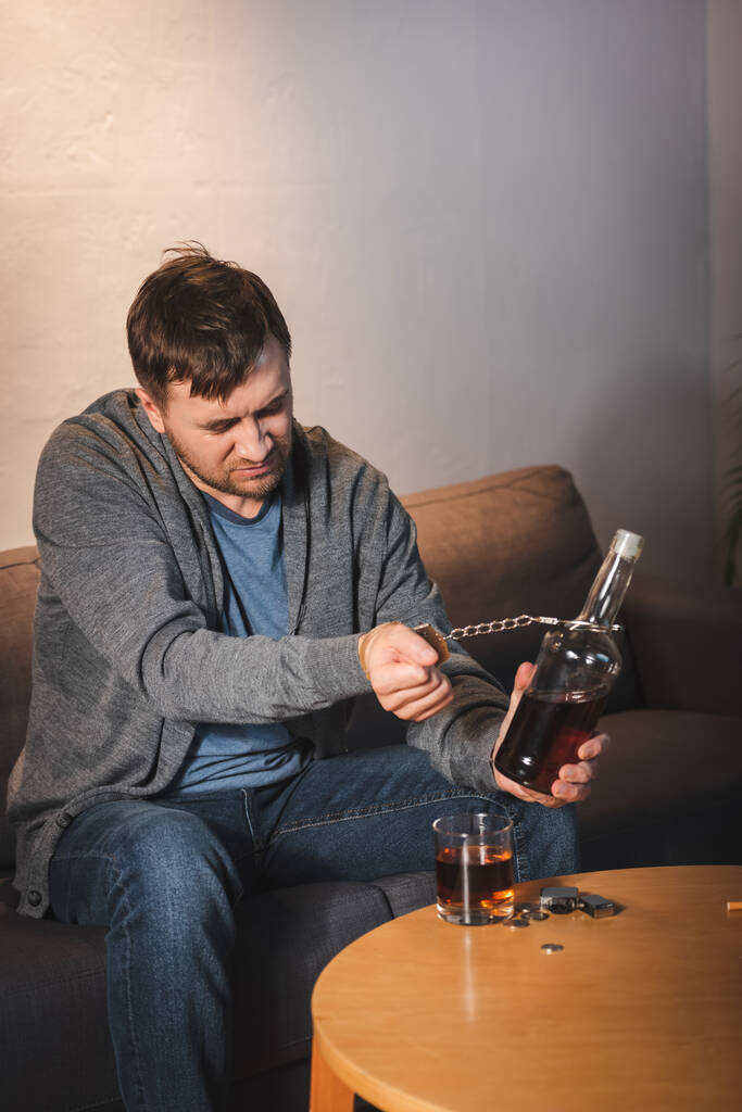alkoholik závislý muž připoutaný k láhvi whisky doma - Fotografie, Obrázek