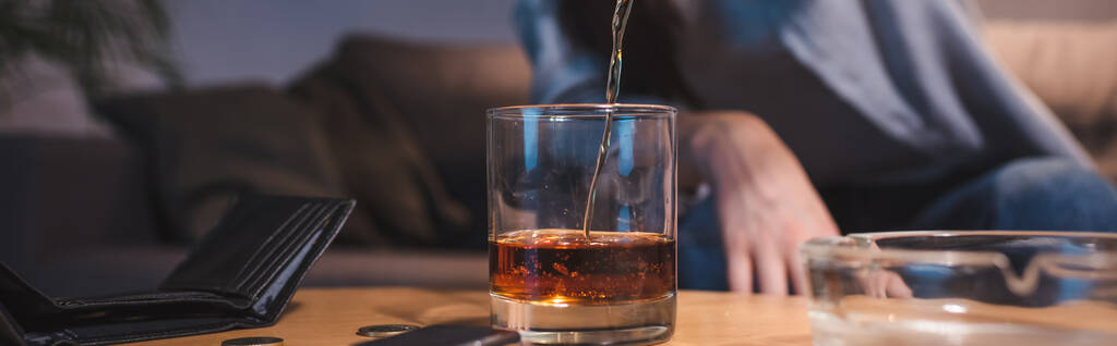 vista ritagliata della donna versando whisky in vetro vicino al portafoglio vuoto, banner - Foto, immagini