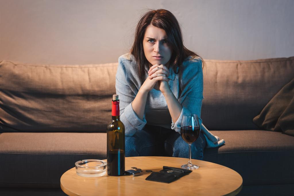 赤ワインとコインと空の財布でテーブルに座っている欲求不満アルコールの女性  - 写真・画像