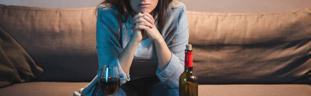 アルコール依存症の女性が瓶や赤ワインのガラスの近くに座っている様子を切り取られ   - 写真・画像