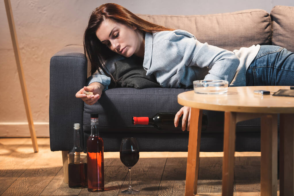 пьяная женщина наливает красное вино в бокал, лежа на диване - Фото, изображение