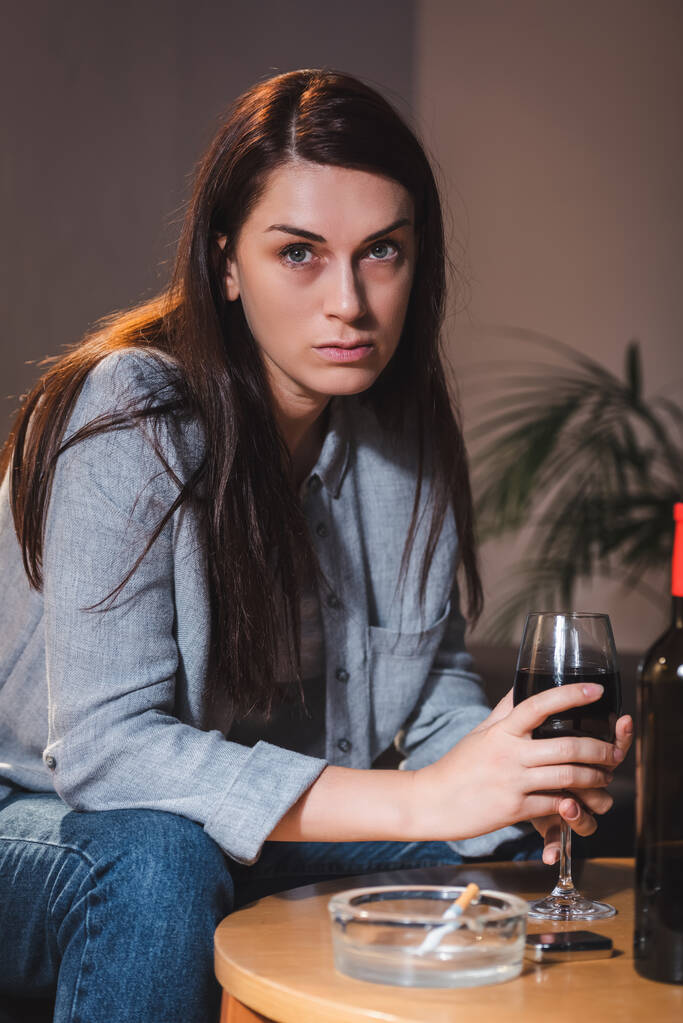 алкогольна жінка дивиться в сторону, сидячи вдома наодинці зі склянкою червоного вина
  - Фото, зображення