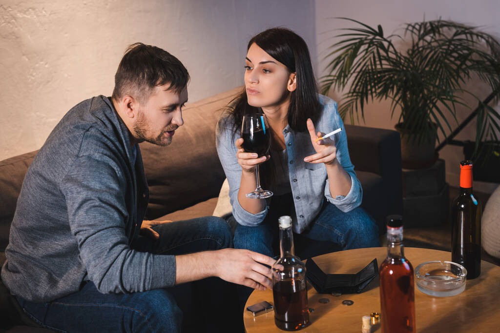 酒に酔った夫と妻が瓶や財布を持ってテーブルに座り - 写真・画像