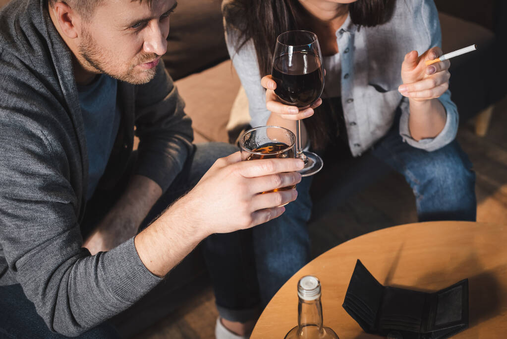alcohol-addicted husband and wife drinking near empty wallet on table - Photo, Image