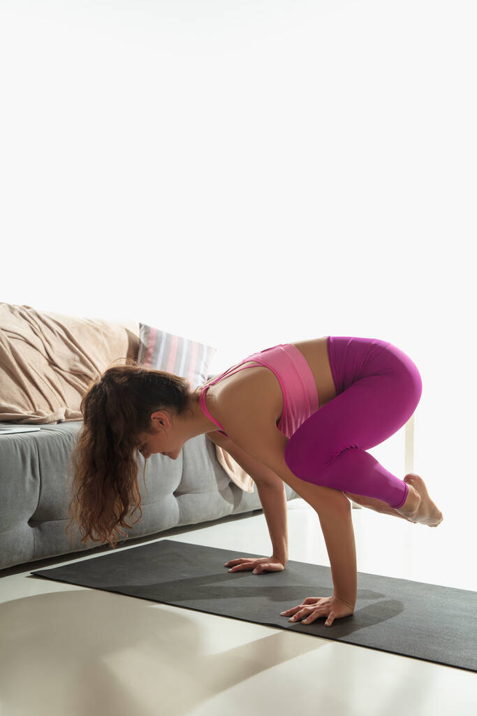 Mooie jonge vrouw uit te werken binnen, doen yoga oefening op grijze mat thuis - Foto, afbeelding