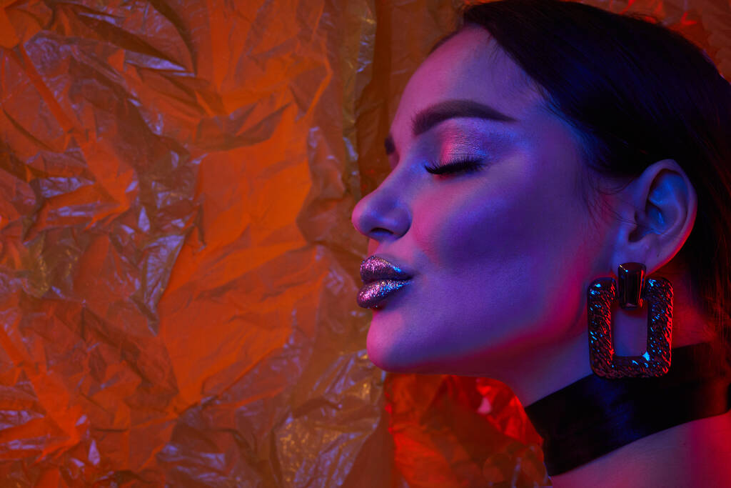 Femme aux lèvres argentées métalliques dans des néons lumineux en studio avec film transparent sur fond. L'art compose. - Photo, image