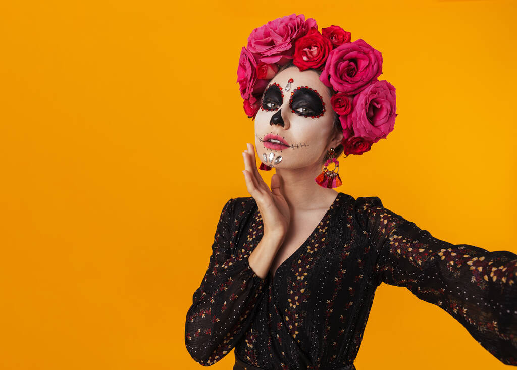 Kaunis tyttö halloween meikki ja kukka seppele ottaen selfie kuva eristetty keltainen seinä - Valokuva, kuva