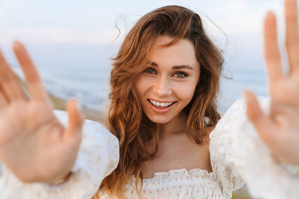 Fiatal kaukázusi vonzó barna nő mosolyog, és mutatja tenyerét a kamera a strandon - Fotó, kép