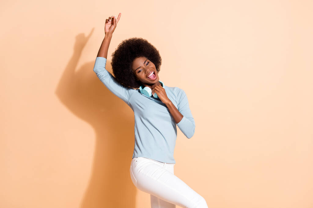 Портрет афро - американської жінки, яка вказує пальцем на бездротові навушники, ізольовані на кольоровому тлі пастеля бежевого кольору. - Фото, зображення