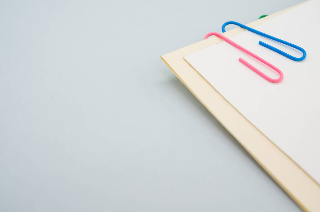Een close-up van een blanco papier met kleurrijke paperclips op een lichtgroene achtergrond - Foto, afbeelding