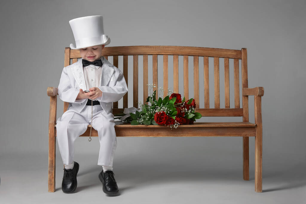 Szczęśliwy chłopczyk w garniturze na ławce z bukietem kwiatów - Zdjęcie, obraz