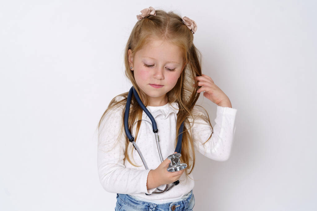 Medicine concept. A girl holds a stethoscope in her hands, plays with it. Isolated over white background. - Photo, Image