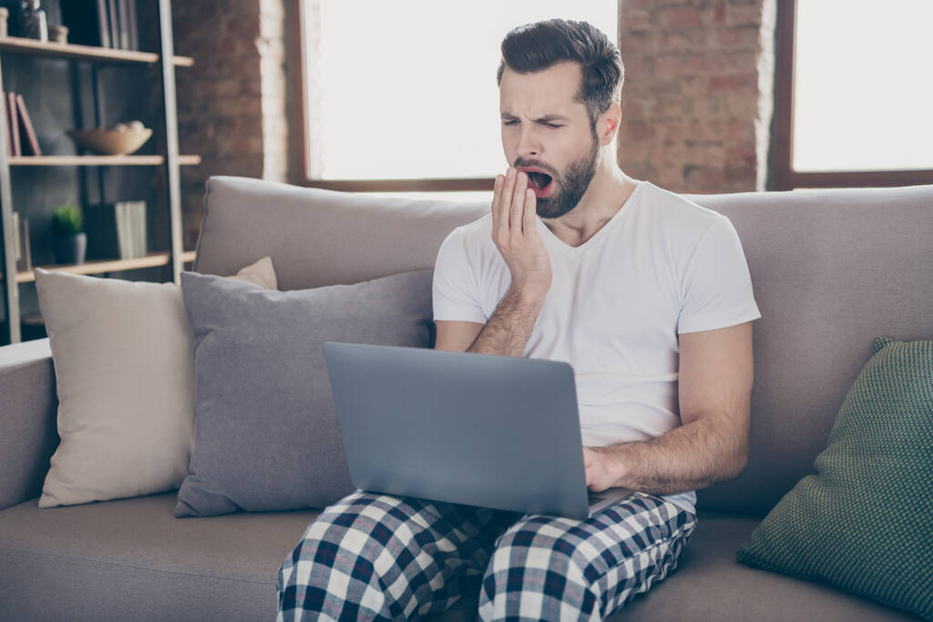 Фото виснаженого чоловіка сидять на роботі дивана віддалений ноутбук втомився підготувати стартап прогрес інноваційний звіт позіхаючий рот ручний одяг нічний одяг в кімнаті в приміщенні
 - Фото, зображення