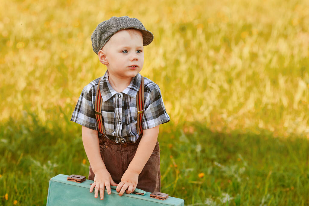 Een mooi klein kind met een koffer op het veld is klaar om te reizen. - Foto, afbeelding