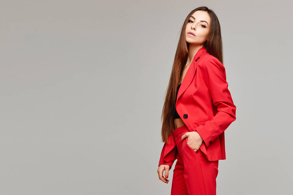 Vista lateral da menina modelo com cabelos longos em terno vermelho elegante isolado no fundo cinza com espaço de cópia - Foto, Imagem
