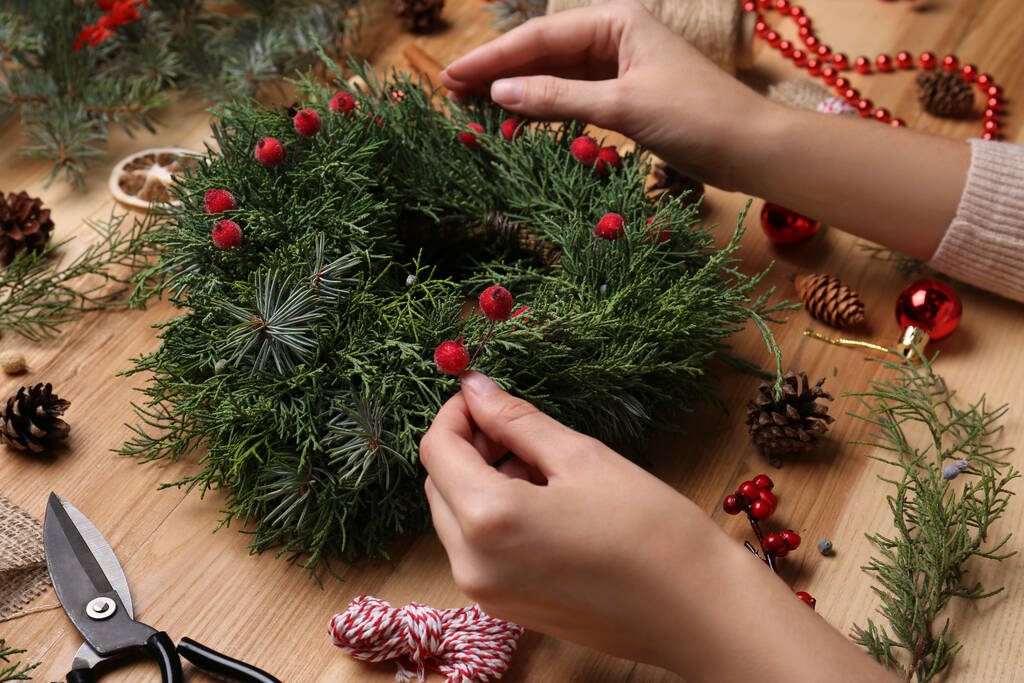 Florist making beautiful Christmas wreath with berries at wooden table, closeup - Photo, Image